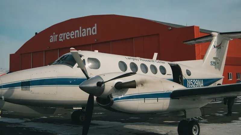 A twin-engine NASA B200 King Air aircraft flying over a dense green forest canopy.