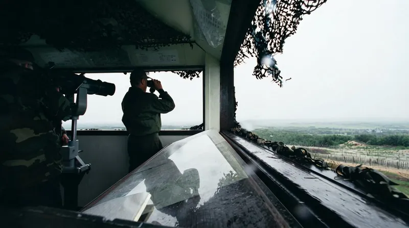 South Korean soldiers stand guard at a barbed wire fence looking out over the Demilitarized Zone.
