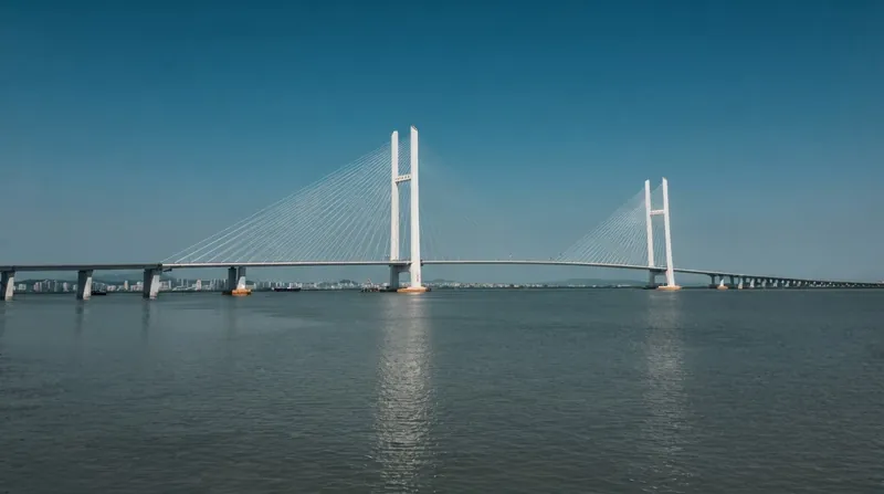A large modern cable-stayed bridge spanning a wide river, connecting a city skyline to a less developed shoreline.