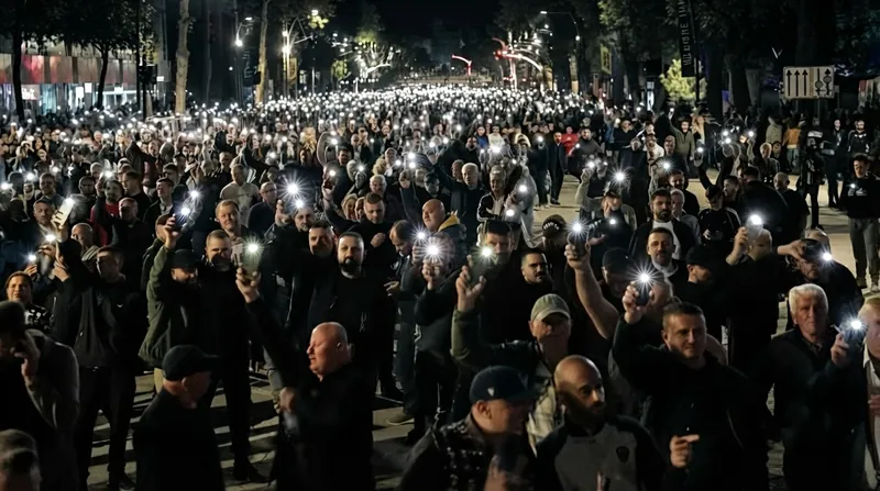 Riot police in gear stand behind shields on a street illuminated by fire and smoke.
